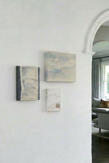 Three abstract paintings on a white wall with an arched doorway into a living room